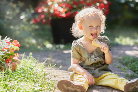 Happy toddler with ice cream is sitting on the grass in in the rays of the sun. Copy spaceの写真素材