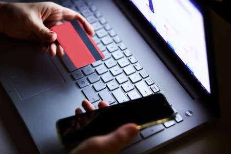 Online shopping. A credit card in his hand near the laptop. Impersonal. Mobile phone for entering text messages.の写真素材