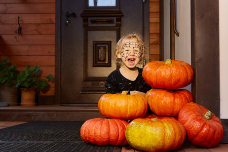 smiling girl is sitting next to pumpkins near the door of the house. halloween decor.の写真素材