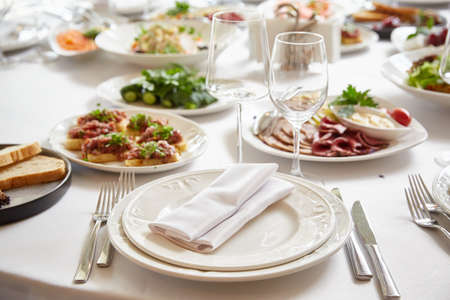 Plates and utensils for food on the festive table. Beautiful glass glasses near plates and festive foodの写真素材