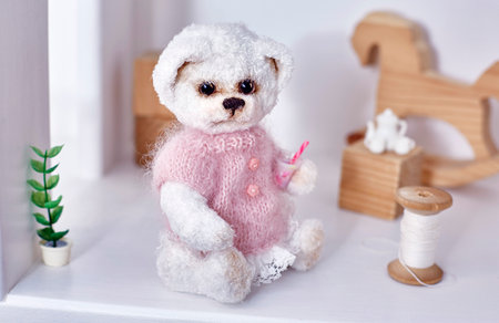 soft toy crocheted wool teddy bear in a pink blouse is sitting in a dollhouse.の写真素材
