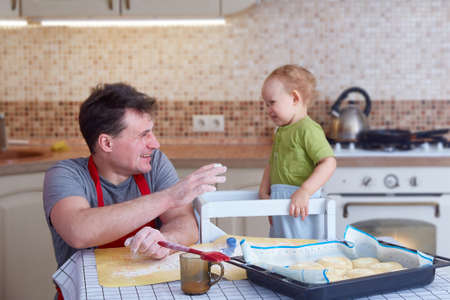 Father has fun playing with a small child while cooking at home in the kitchen. Fatherhood and parenthood concept.の写真素材