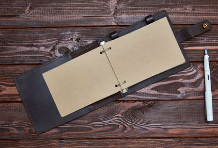 notebook with craft paper in an unfolded form lies on a wooden surface with a white fountain pen.の写真素材