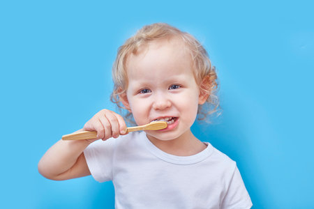 curly-haired girl brushes her teeth with a wooden toothbrush on a blue background with copies space. The concept of recycling and eco friendlyの写真素材
