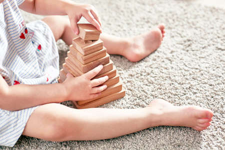 outface child is playing a wooden pyramid while sitting on a carpet.の写真素材