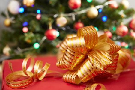Close-up of a gift box decorated with a golden ribbon bow under a Christmas tree on Christmas or New Yearの写真素材
