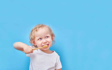 Child brushes his teeth with a wooden bamboo toothbrush on a blue background with a copy space.の写真素材