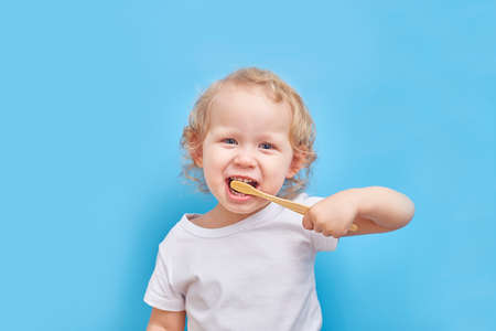 left-handed child brushes his teeth with a bamboo toothbrush on a plain background with a place for textの写真素材