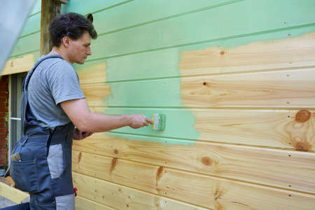 man in a workers suit is painting the wooden surface of the wall green.の写真素材