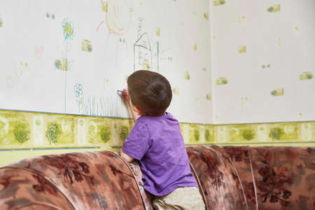 kid draws on the wallpaper standing on the sofa in the living room. close-up. The concept of self-isolation during the pandemicの写真素材