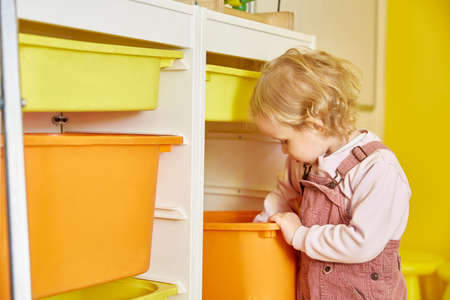 curly-haired girl is digging in a box with toys.の写真素材