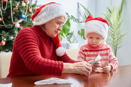 Grandma and granddaughter in Santa hats make crafts for the Christmas tree on Christmas Eve.の写真素材