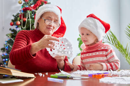surprised girl looks at her grandmothers crafts for the new year and Christmas. Santas hat as a symbol of Christmasの写真素材
