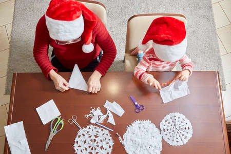 child and an adult are preparing for the new year and Christmas by cutting out decorative snowflakes from napkins. top view.の写真素材