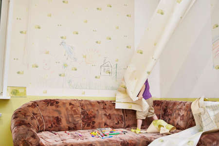 child rejoicing tears the wallpaper off the wall of the house during a lockdown.の写真素材