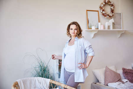 young girl with a pregnant belly is standing in the bedroom near the bed.の写真素材