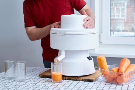faceless man squeezes carrot juice in a white professional juicer.の写真素材