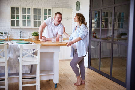 husband and a pregnant wife are laughing merrily at home in the kitchen. The concept of happy motherhood and family.の写真素材
