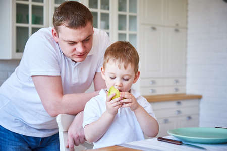 Dad and a little boy in the kitchen. The son has a yellow apple.の写真素材