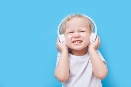 child wearing headphones and a white T-shirt listens to music on a blue background with a place for text.の写真素材