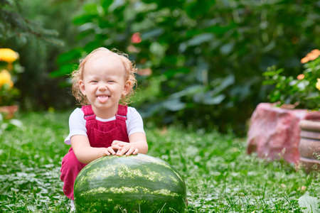child cheerfully shows his tongue with a watermelon in his hands. Health, walking, healthy food. Picnic in the gardenの写真素材
