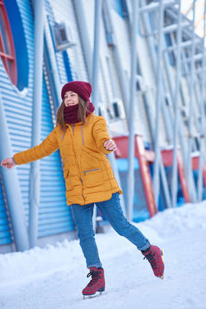 young woman in a red hat and a yellow jacket is ice skating at the stadium on a frosty winter day. Vertical frame.の写真素材