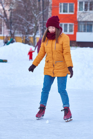 young woman in a yellow jacket rides on ice on a lake in the courtyard of multi-storey buildings. Vertical frameの写真素材