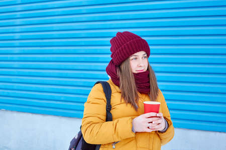 young woman with a disposable cup of coffee on a blue background.の写真素材