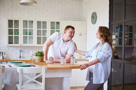 cheerful husband and a pregnant wife are laughing in the kitchen of their big bright house.の写真素材