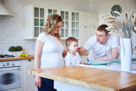family with a small boy and a pregnant young woman in the kitchen.の写真素材