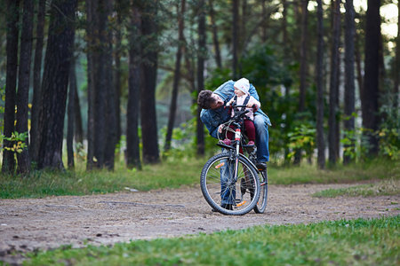 child girl and father ride a bike in the park. Cycling holidays and active weekends. Kids are sitting in a basket on a bicycle. Summer family day.の写真素材