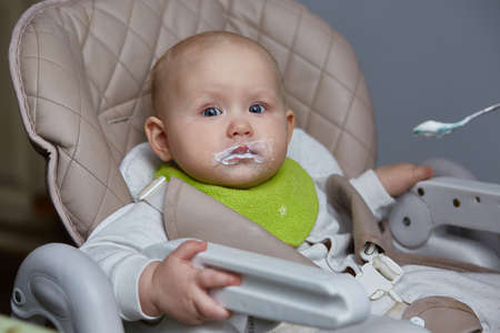 Portrait of a baby eating in a high chair for the first time with a spoonの写真素材
