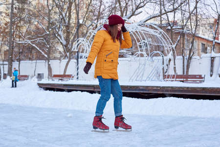 woman in a yellow jacket and a red hat is skating in winter.の写真素材