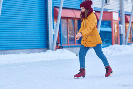woman in a yellow jacket skates against the background of a blue sports buildingの写真素材