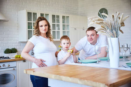family with a small child and a pregnant woman in the kitchen.の写真素材