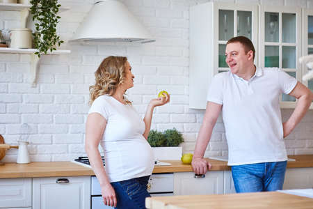 Pregnant woman and her husband in the kitchen at home with fruit.の写真素材