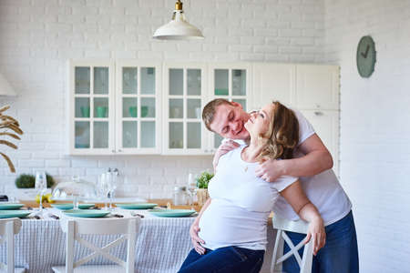 happy family with pregnant woman sitting in scandinavian kitchen and having fun. Copy space.の写真素材