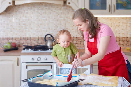 A young woman teaches a child to cook pastries. Greases the pies in the baking tray with a cooking brush.の写真素材
