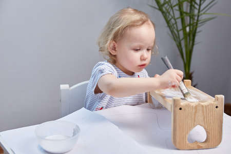 girl paints a wooden dolls crib with a brush. Childrens creativity. Childrens hobbies.の写真素材