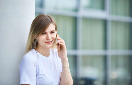 Beautiful caucasian young woman is talking on the phone on the street in the city on a summer day. Close-up.の写真素材