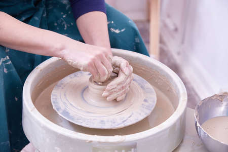 hands of a ceramist make dishes on a potters wheel.
