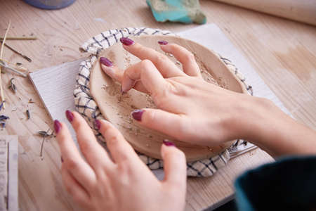 female hands of a ceramist smooth out a figured plate or panel.
