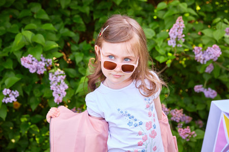 fashionable little girl in sunglasses walks through a blooming garden.の写真素材