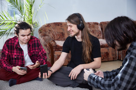 Millennials guys communicate sitting on the carpet with smartphones in their hands.
