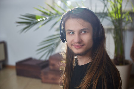 Portrait of a young man with long hair wearing headphones at homeの写真素材