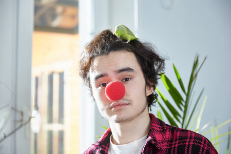 The unlucky birthday of a young man is saddened and disappointed that no one came to celebrate his anniversary. Pet parrot on the head. Red clown nose.の写真素材