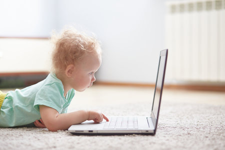 small child at a computer lying on a carpet in a living room.の写真素材