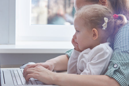 The child is in the arms of a mother working on a laptop at home. The concept of freelancing and working from home with children. Copy space.の写真素材
