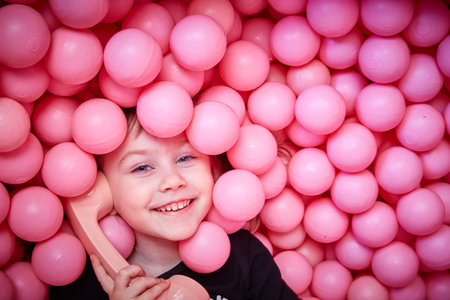 A cheerful girl with a retro handset in her hands lies in the pink balls of a dry pool.の写真素材