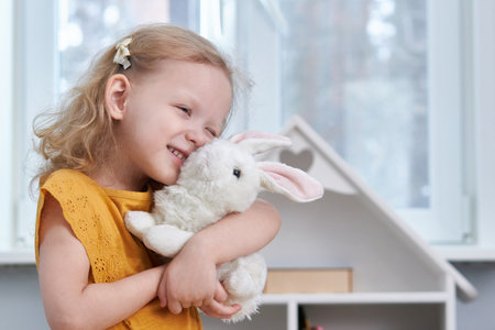 Smiling girl hugs a white rabbit toy. The concept of reconciliation and love. Copy Spaceの写真素材